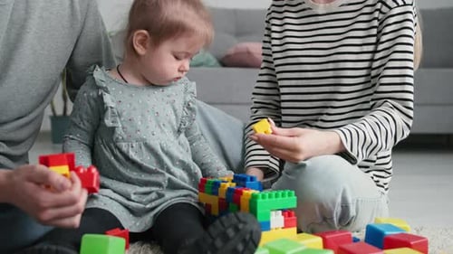 Sorglose Kindheit kleines süßes Mädchen spielt mit ihren Eltern mit farbigem Kunststoffkonstruktor