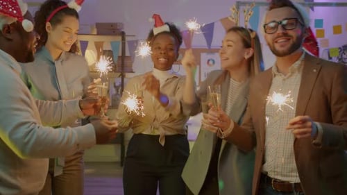 Joyful Colleagues Dancing Clinking Champagne Glasses Holding Bengal Lights in Dark Office