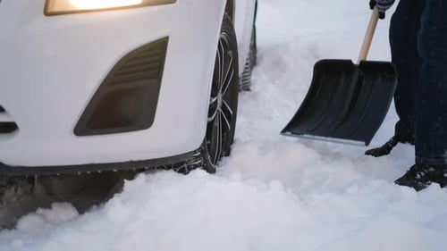 Person Shoveling Snow from Around Car Tire in Winter