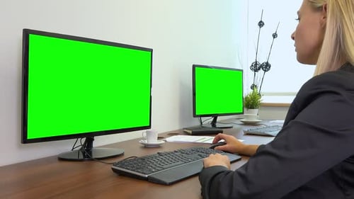 An Office Worker Sits at A Desk and Works on A Computer with A Green Screen