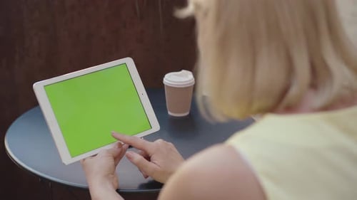 Unrecognizable Woman Holding Tablet with Chromakey Screen Outdoors and Drinking Coffee. Blond