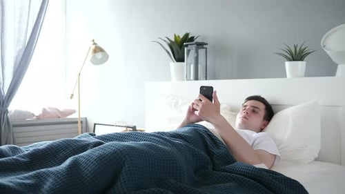 Man Using Smartphone while Lying in Bed