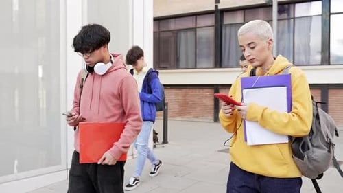 Young Adults Walking on Sidewalk with Books and Phones