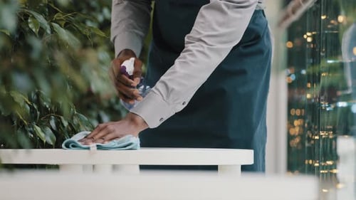 Young Unrecognizable African American Male Waiter in Apron Catering Worker Wipes Table in Cafe