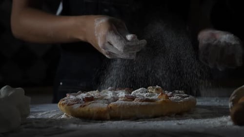 Movimiento lento de las manos de una mujer tamizando la harina sobre la pizza