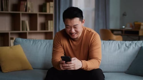 Man Smiling Using Smartphone While Sitting on Couch