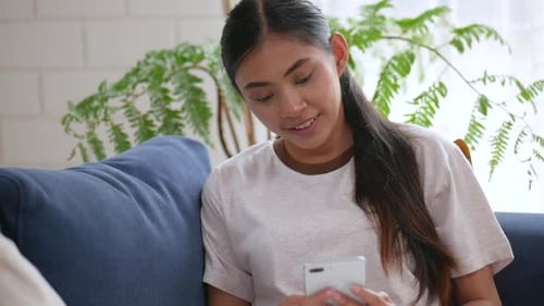 Young Woman Using Smartphone While Relaxing on Couch