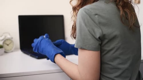 Woman Sanitizing Laptop With Gloves and Disinfectant