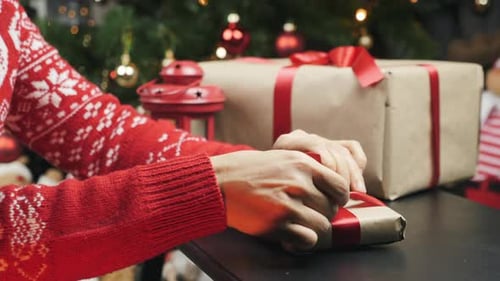 Person Wrapping Christmas Gift with Red Ribbon