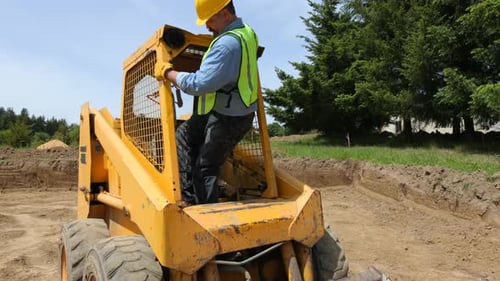 Man climbs into yellow skid steer loader