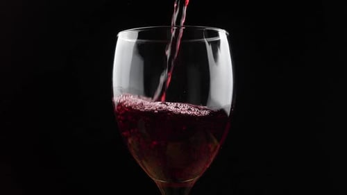 Wine. Red wine pouring in wine glass over dark background.