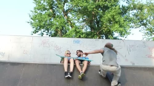 Skateboarder jumping over friends on ramp in skateboard park
