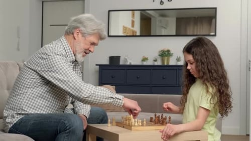 Happy Grandfather Teaches His Granddaughter to Play Chess at Home in the Living Room