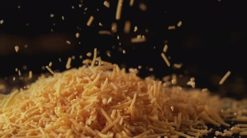Die Kamera folgt zerkleinertem Cheddar-Käse. Zeitlupe.