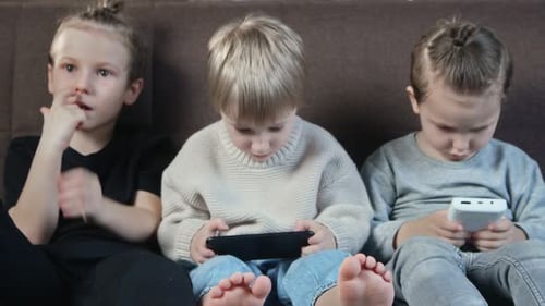 Three Children Relaxing on Couch with Mobile Devices