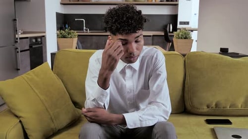 Cansado de raza mixta sentado en el sofá siente dolor en los ojos