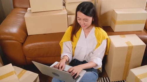 Woman Working on Laptop Surrounded by Boxes