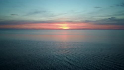 Drohne fliegt in einem wunderschönen Sonnenuntergang rückwärts über das Meer. Bunter Sonnenuntergang an der Ostsee, Lettland