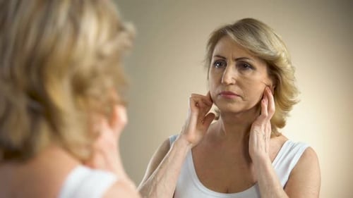 Woman Looks in Mirror, Touches Face