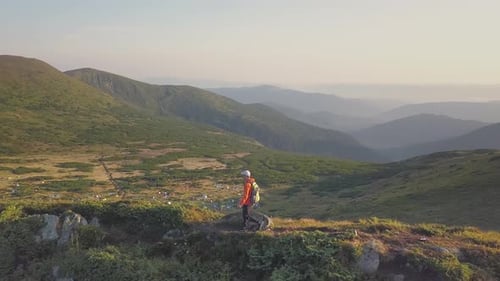 Tourist hiker with a backpack in orange jacket walking on mountain path in Carpathian mountains.
