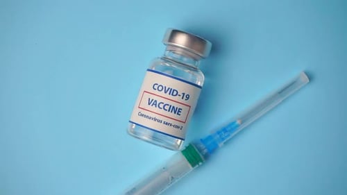 COVID-19 vaccine vial and syringe on blue surface