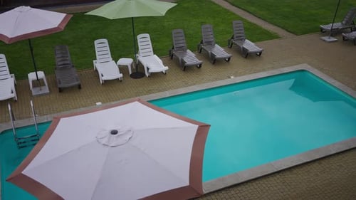 Top View Parasol on Poolside with Blue Swimming Pool and Deck Chairs with No People Outdoors