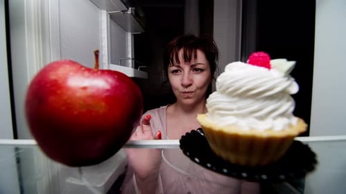Woman Choosing Cupcake over Apple in Refrigerator
