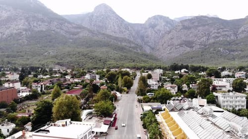 Aerial View of a Beautiful Town Among Trees at the Foot of the Mountains and Busy Traffic on the