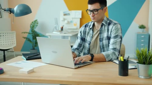 Serious Guy Using Laptop Typing Sitting at Table in Office Concentrated on Job