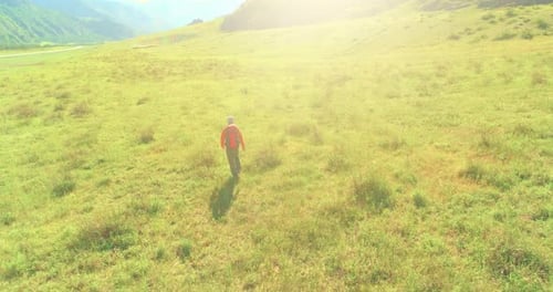 Flight Over Backpack Hiking Tourist Walking Across Green Mountain Field. Huge Rural Valley at Summer