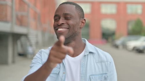 Smiling Man Points at Camera in Urban Setting