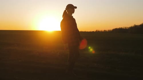 Farmer Girl Walking Beside Green Wheat Field Enjoying the Sun. Female Farmer in Plaid Shirt and Hat