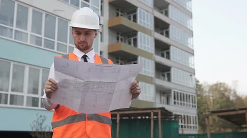 Un ingeniero civil en un sitio de construcción examina los planos de construcción.