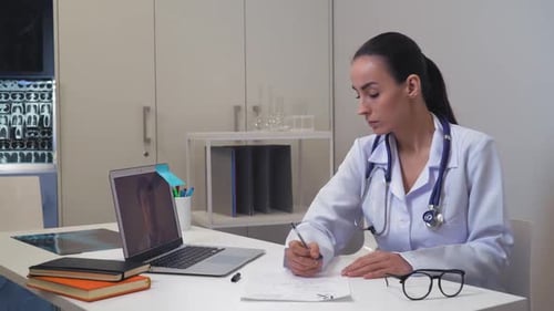 Woman Doctor Writing at Desk in Office