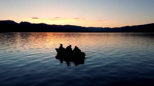 Person pull starting motor of boat floating on lake at sunset