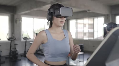 4K Asian athletic woman in sportswear wearing VR glasses jogging on treadmill at fitness gym.