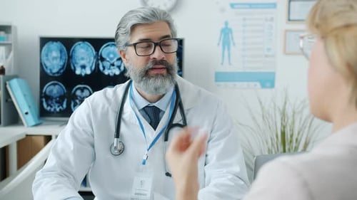 Experienced Doctor Listening to Female Patient Giving Advice Writing Prescription in Hospital