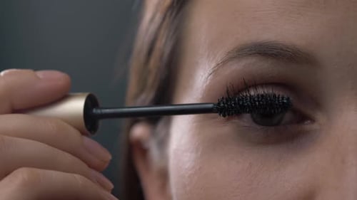 Close Up Shot of Young Woman Applying Mascara on Eyelashes Against Black Background