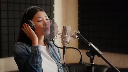 Talentierte asiatische Sängerin trägt Kopfhörer und singt im Studio Song to Mic