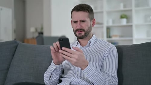 Upset Man Reacting to Phone on Couch