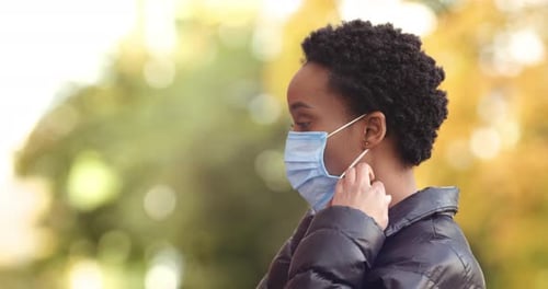Young Woman Puts on Surgical Mask Outdoors