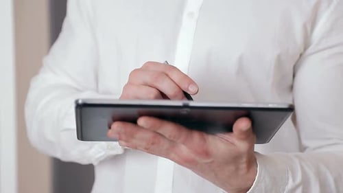 Close-up of a Businessman's Hand Holding a Stylus in His Hand and Working on a Tablet