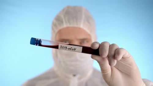 Mann im Schutzanzug, medizinische Maske, Handschuhe zeigt Reagenzglas mit Coronovirus