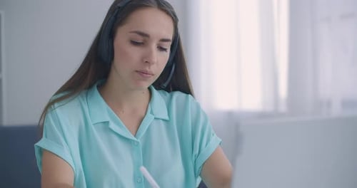 Woman with Headset Works at Computer Taking Notes