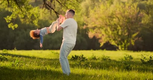Loving Father lächelt beim Gehen mit dem Kind, das bei Sonnenuntergang auf einer Wiese im Sommer auf dem Hals sitzt