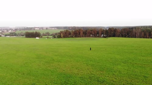 Aerial View of a Young Girl Running Across a Huge Green Field Against the Backdrop of a Rural