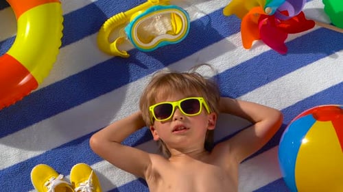 Boy Lies on Beach Towel with Summer Gear