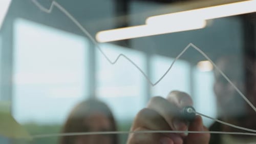 Closeup Shot of Concentrated Man Analyst Standing in Front of Glass Wall and Tracing Lines on