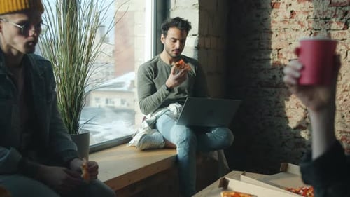 Diverse Group of Businessmen Eating Pizza in Office Talking and Using Laptop Computer in Day Time