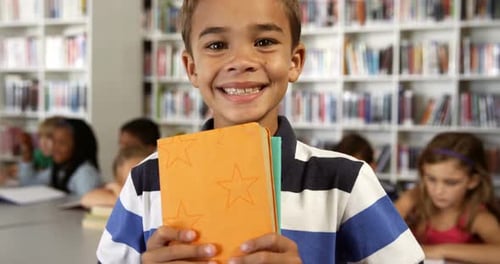 Portrait of schoolboy holding books in library